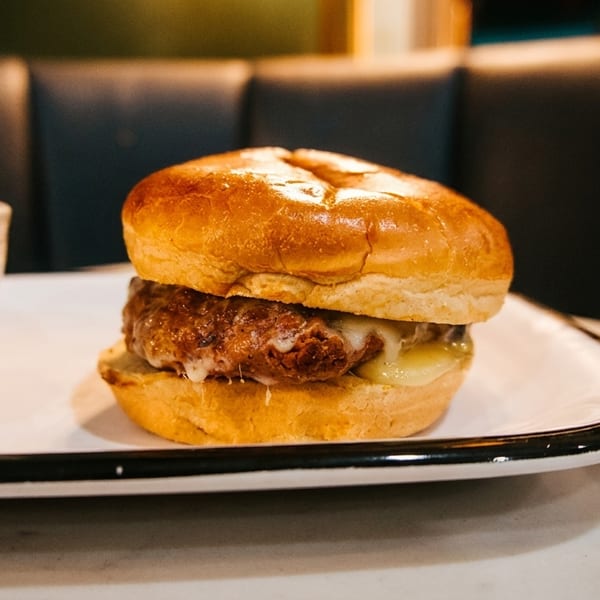 Cheesy burger and a bowl of golden fries on a white plate in a restaurant setting.